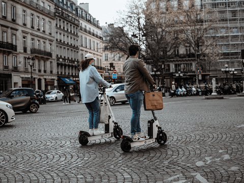 a couple riding electric scooters on a cobbled street