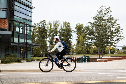 a cyclist rides an electric bike on the road past buildings and trees