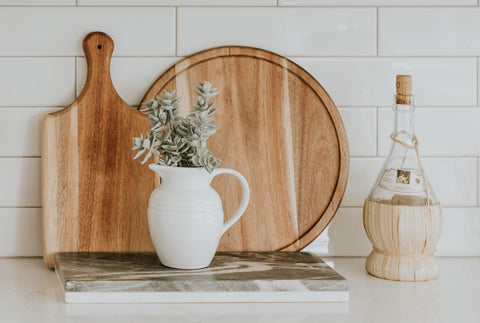 an assortment of minimalist sustainable homeware including wooden chopping boards, a glass bottle and eucalyptus in a white jug
